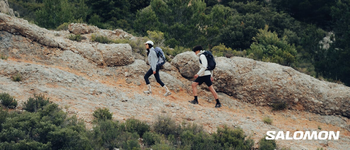 Zwei Wanderer steigen mit Rucksäcken über einen felsigen Bergtrail inmitten von Natur