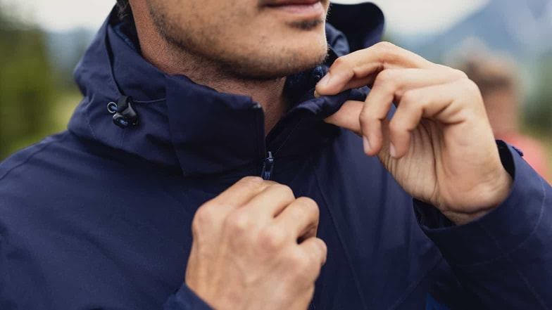 Wanderer schließt den Reißverschluss seiner Hardshelljacke.