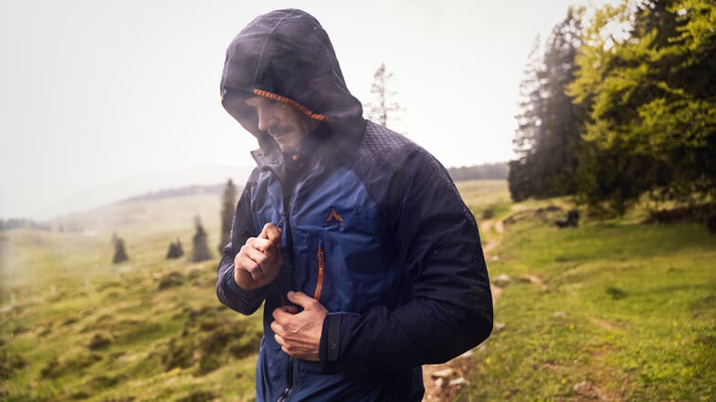 Muž v dešti si zapíná modrou hardshellovou bundu.