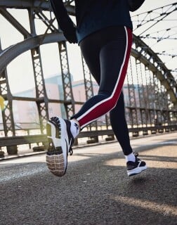 Nahaufnahme von laufenden Beinen in Sportkleidung auf einer Brücke.