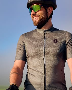 Ein Mann mit Scott Radbekleidung schaut lächelnd in Richtung Sonnenuntergang.