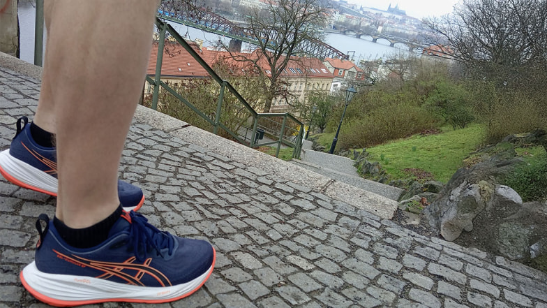 Detail běžeckých bot Asics Gel Cumulus 27 s výhledem na Prahu a Vltavu.