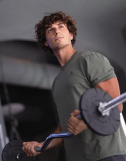 Muž zvedá činku v posilovně.