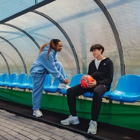 Ein junger Mann und eine junge Frau unterhalten sich am Rande eines Fußballfelds.