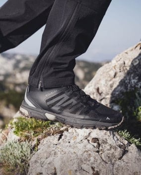 Wanderschuh mit Profilsohle steht auf einem Felsen in bergiger Umgebung.