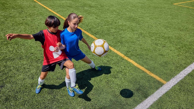 Ein Junge und ein Mädchen versuchen am Fußballfeld an den Ball zu kommen.