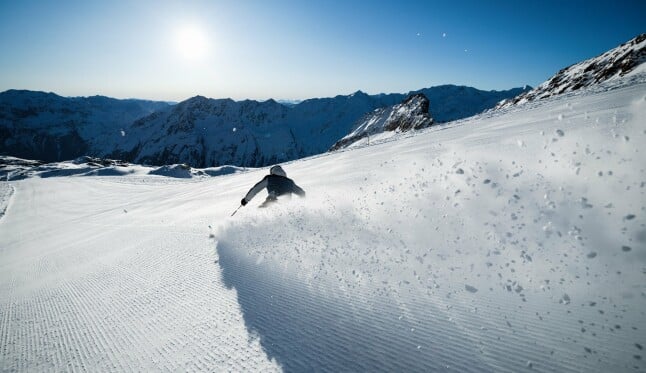 Ein Skifahrer carvt eine Piste bei strahlendem Sonnenschein hinunter.