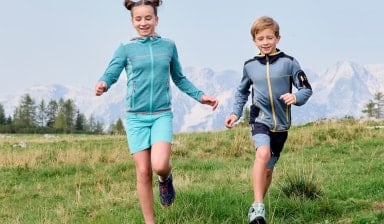 Zwei Kinder laufen glücklich auf einer Wiese in den Bergen.