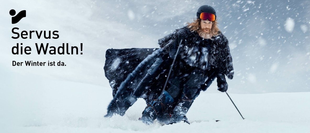 Der Winter (bärtiger Mann mit Pelzumhang) fährt Ski bei Schneefall.