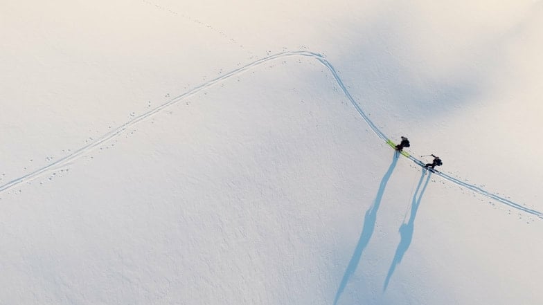 Luftaufnahme von zwei Skitourengehern, die Spuren im Schnee hinterlassen.