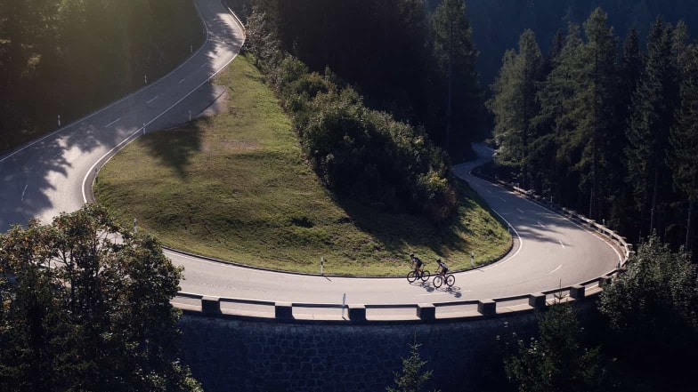 Eine einsame Straße in den Bergen bei Sonnenuntergang mit zwei Rennradfahrern.