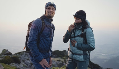 Zwei Wanderer mit Stirnlampen auf einem Berg bei Sonnenaufgang.