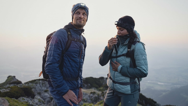 Zwei Wanderer mit Stirnlampen auf einem Berg bei Sonnenaufgang.