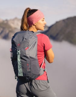 Žena zezadu v outdoorovém oblečení a s batohem kouká směrem na výhled na hory.