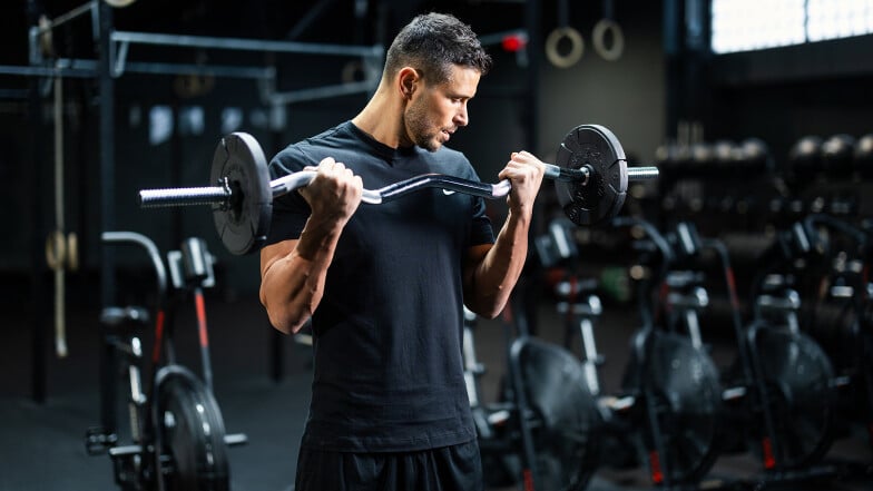 Ein muskulöser Mann macht Bizeps-Curls mit einer Hantel im Fitnessstudio.