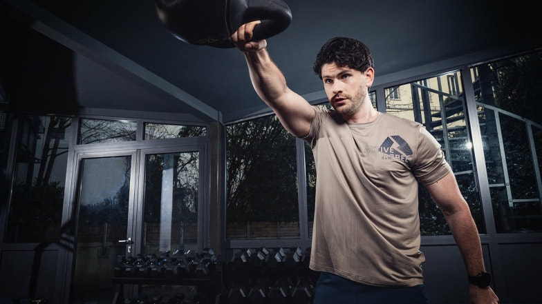 Ein Mann trainiert mit einer Kettlebell in einem  Fitnessraum.
