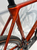Nahaufnahme des Rahmens eines orangefarbenen Fahrrads mit sichtbaren Schrauben und Reifen.