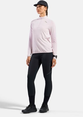 Eine Frau in einem rosafarbenen Langarmshirt und schwarzen Leggings vor weißem Hintergrund.