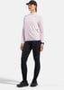Eine Frau in einem rosafarbenen Langarmshirt und schwarzen Leggings vor weißem Hintergrund.