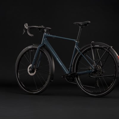 Dunkelblaues Gravelbike mit Schutzblechen und Gepäckträger vor schwarzem Hintergrund. Dunkelblaues Gravelbike mit Schutzblechen und Gepäckträger vor schwarzem Hintergrund.