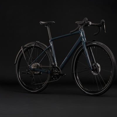 Ein dunkelblaues Gravelbike mit Schutzblechen und Gepäckträger vor schwarzem Hintergrund. Ein dunkelblaues Gravelbike mit Schutzblechen und Gepäckträger vor schwarzem Hintergrund.