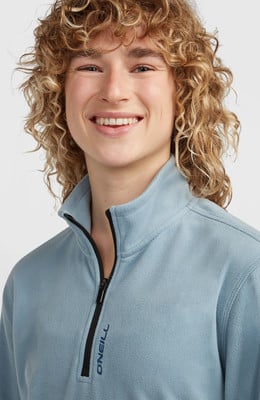 Ein junger Mensch mit lockigem Haar und einem Lächeln trägt einen blauen Fleece-Pullover. Ein junger Mensch mit lockigem Haar und einem Lächeln trägt einen blauen Fleece-Pullover.