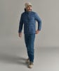 Ein Mann in einer blauen Daunenjacke und Skischuhen lächelt.