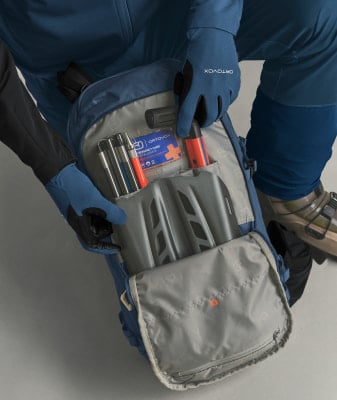 Eine Person verstaut eine Lawinensonde und eine Schaufel in einem Rucksack. Eine Person verstaut eine Lawinensonde und eine Schaufel in einem Rucksack.