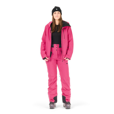 Eine Frau in einer rosa Skijacke, Hose und schwarzer Mütze posiert vor weißem Hintergrund. Eine Frau in einer rosa Skijacke, Hose und schwarzer Mütze posiert vor weißem Hintergrund.