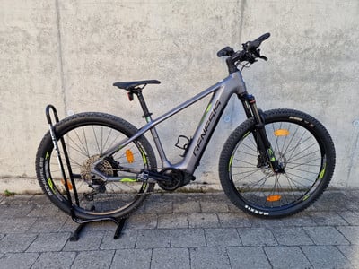 Graues Genesis E-Bike mit Federung und breiten Reifen auf einem Ständer.