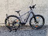 Graues Genesis E-Bike mit Federung und breiten Reifen auf einem Ständer.