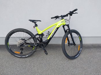 Grünes Mountain-Elektrofahrrad mit Federung, das an einer Wand geparkt ist.
