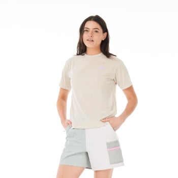 Eine Frau in einem beigen T-Shirt und bunten Shorts steht mit den Händen in den Hüften.