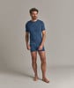 Ein Mann in einem blauen T-Shirt und Unterwäsche steht vor einem grauen Hintergrund.