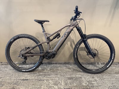 Ein graues E-Bike mit Federung und schwarzen Rädern steht auf dem Boden. Ein graues E-Bike mit Federung und schwarzen Rädern steht auf dem Boden.
