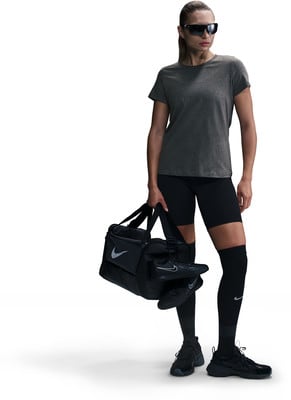 Eine Frau in Sportkleidung hält eine schwarze Tasche mit Schuhen.