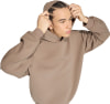 Ein junger Mann im braunen Hoodie richtet seine Haare.