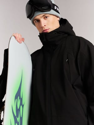 Ein Mann in einer Skijacke hält ein Snowboard mit grünem Flammenmuster. Ein Mann in einer Skijacke hält ein Snowboard mit grünem Flammenmuster.