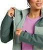 Eine Frau schließt den Reißverschluss einer grünen Jacke mit einem rosa T-Shirt darunter.