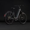 Graues Cube E-Bike mit Gepäckträger und Schutzblechen vor schwarzem Hintergrund.