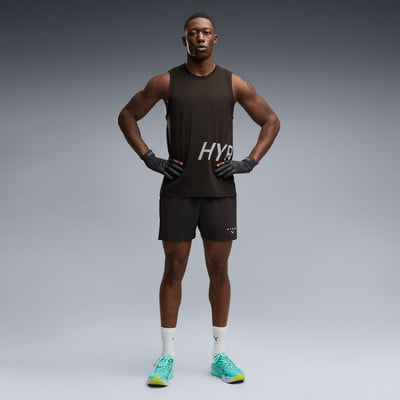 Ein Mann in schwarzem Tanktop und Shorts posiert mit Händen in den Hüften.