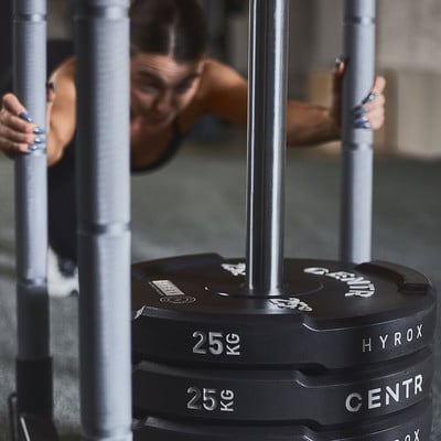 Eine Frau schiebt einen Schlitten mit Gewichten im Fitnessstudio, Fokus auf die Gewichte.