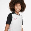 Junge in einem weißen T-Shirt mit schwarzen Ärmeln und einem rosa Nike-Logo.
