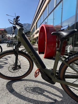 Ein grünes Cube E-Bike steht vor einem modernen Gebäude mit großen Fenstern.