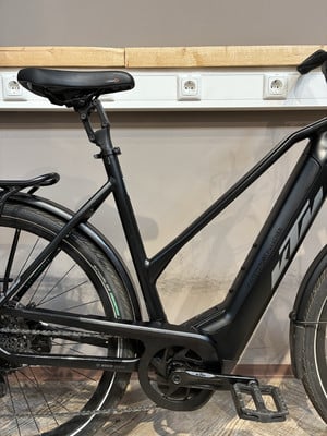 Ein schwarzes KTM E-Bike mit Schutzblechen und Ständer steht auf Holzboden. Ein schwarzes KTM E-Bike mit Schutzblechen und Ständer steht auf Holzboden.