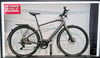 Graues Herren-E-Bike mit Ständer und Logo an der Wand.