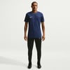 Ein Mann in einem dunkelblauen Nike-T-Shirt und schwarzer Hose steht.