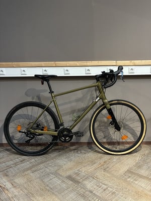 Ein grünes Gravelbike steht auf einem Holzboden vor einer grauen Wand. Ein grünes Gravelbike steht auf einem Holzboden vor einer grauen Wand.