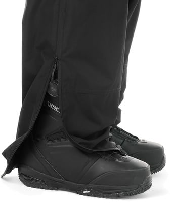 Detail einer Hose mit geöffnetem Reißverschluss und Snowboardschuhen.