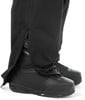 Detail einer Hose mit geöffnetem Reißverschluss und Snowboardschuhen.